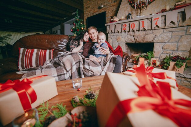 Familia sentada en el sofá arropada con una manta y visto desde los regalos marrones de la mesa