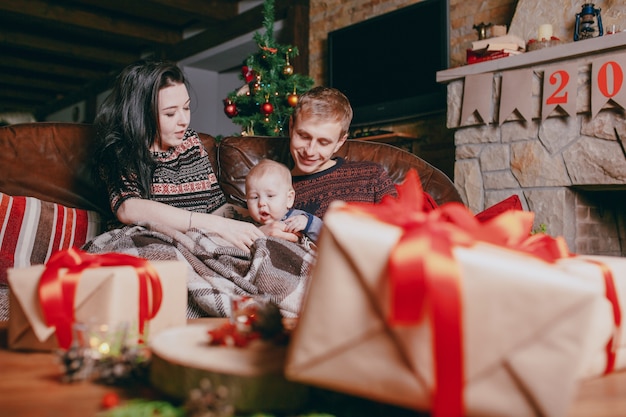 Familia sentada en el sofá arropada con una manta y visto desde los regalos marrones de la mesa