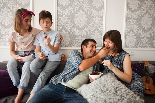 Familia sentada en el sofá y disfrutando de la fresa en casa.