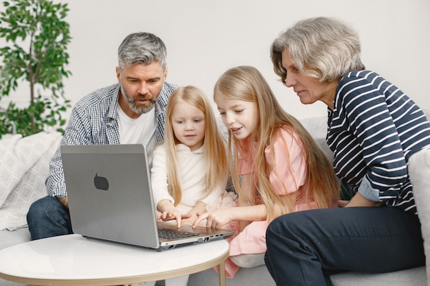 Familia sentada en el sofá. El hombre y la mujer maduros juegan con sus nietas en la computadora portátil. Concepto de tecnologías.