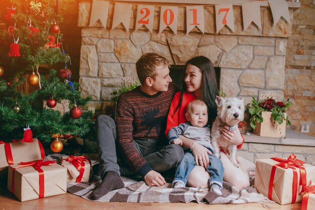 Familia sentada en el suelo con regalos marrones y un árbol de navidad