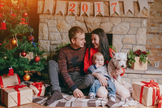 Familia sentada en el suelo con regalos marrones y un árbol de navidad