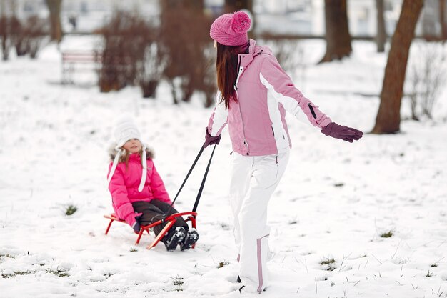 Familia con sombreros de invierno tejidos en vacaciones familiares de Navidad. Mujer y niña en un parque. Gente jugando con trineo.