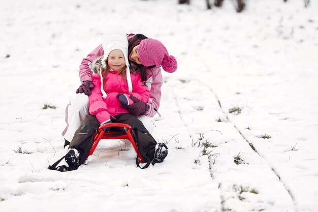 Familia con sombreros de invierno tejidos en vacaciones familiares de Navidad. Mujer y niña en un parque. Gente jugando con trineo.