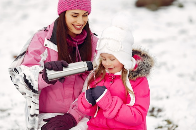 Familia con sombreros de invierno tejidos en vacaciones familiares de Navidad. Mujer y niña en un parque. Gente con termo.