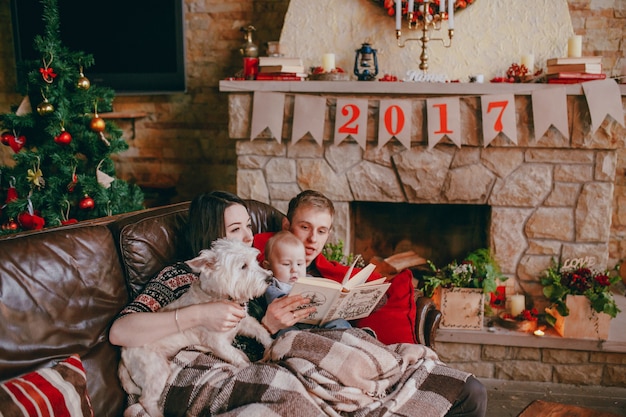 Foto gratuita familia sonriendo en un sofá con un libro en las manos del padre y una chimenea de fondo con el cartel 