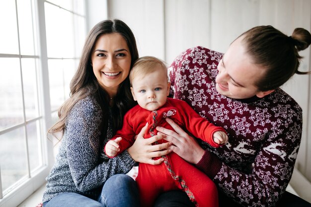 Familia sonriente feliz en el estudio en el fondo del árbol de navidad con el regalo