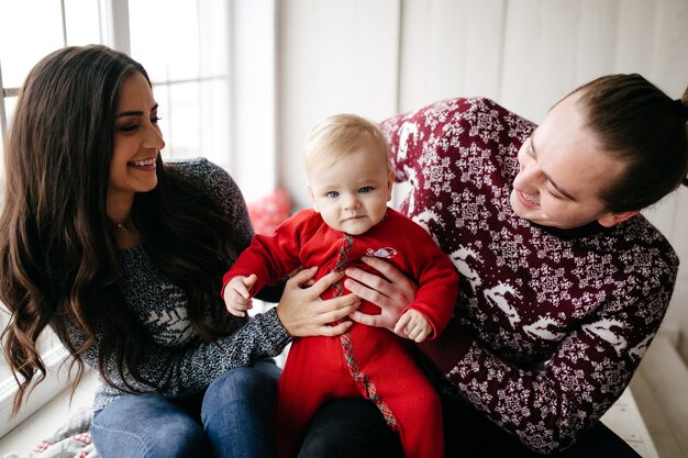 Familia sonriente feliz en el estudio en el fondo del árbol de navidad con el regalo