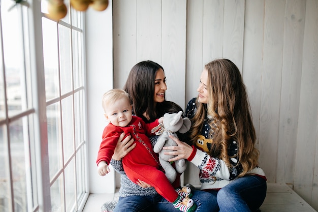 Familia sonriente feliz en el estudio en el fondo del árbol de navidad con el regalo