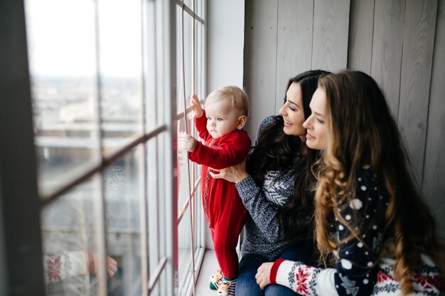 Familia sonriente feliz en el estudio en el fondo del árbol de navidad con el regalo