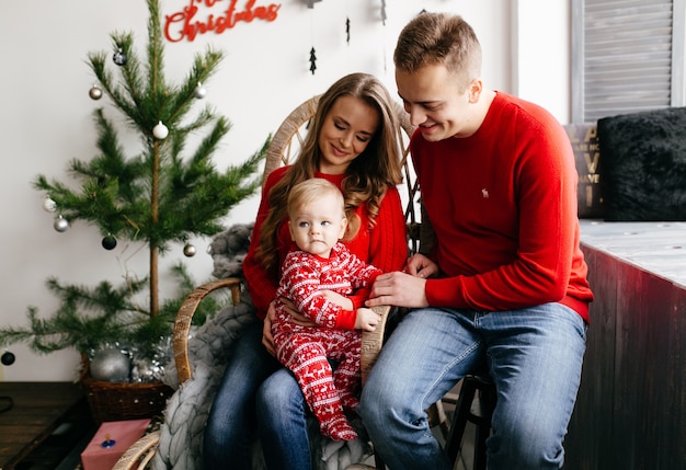 Familia sonriente feliz en el estudio en el fondo del árbol de navidad con el regalo