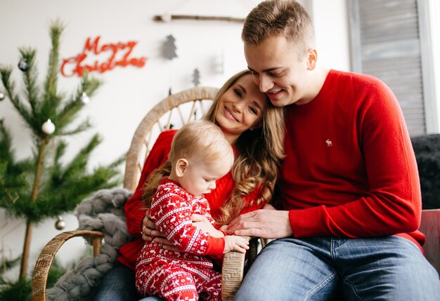 Familia sonriente feliz en el estudio en el fondo del árbol de navidad con el regalo