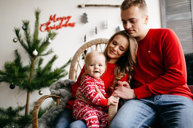 Familia sonriente feliz en el estudio en el fondo del árbol de navidad con el regalo