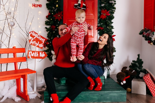 Familia sonriente feliz en el estudio en el fondo del árbol de navidad con el regalo