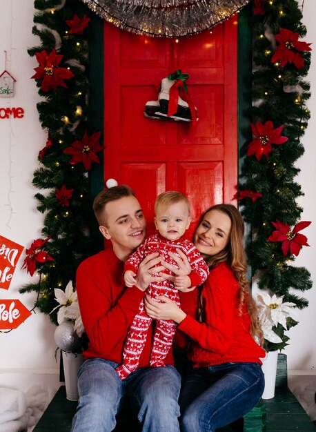 Familia sonriente feliz en el estudio en el fondo del árbol de navidad con el regalo