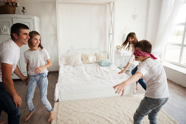 Familia sonriente jugando aficionado ciego en dormitorio