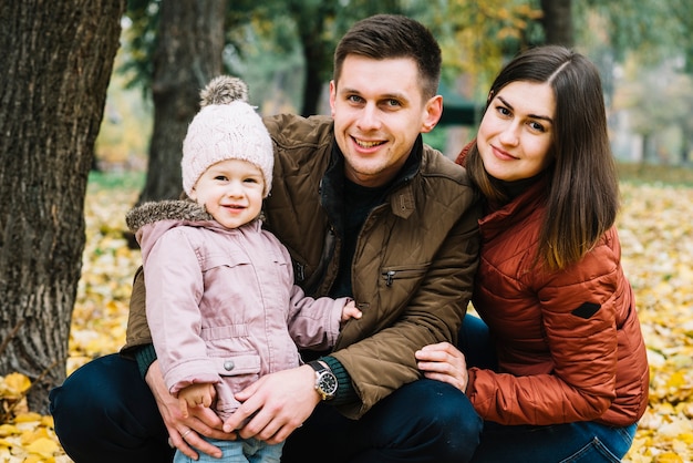 Familia sonriente con la pequeña hija en el parque de otoño