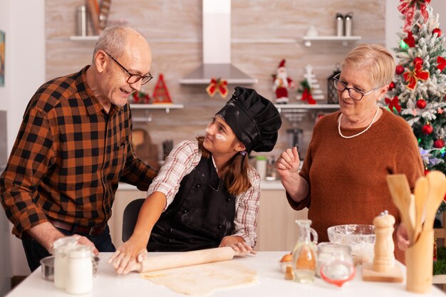 Familia sonriente de pie a la mesa en la cocina culinaria decorada de Navidad celebrando las vacaciones de Navidad