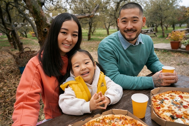 Foto gratuita familia sonriente de tiro medio comiendo pizza al aire libre