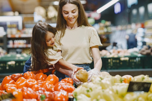 Familia en el supermercado. Mujer con camiseta marrón. La gente elige verduras. Madre con hija.