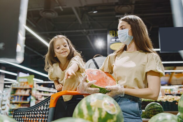 Familia en el supermercado. Mujer con máscara protectora. La gente elige verduras. Madre con hija. Coronavirus.