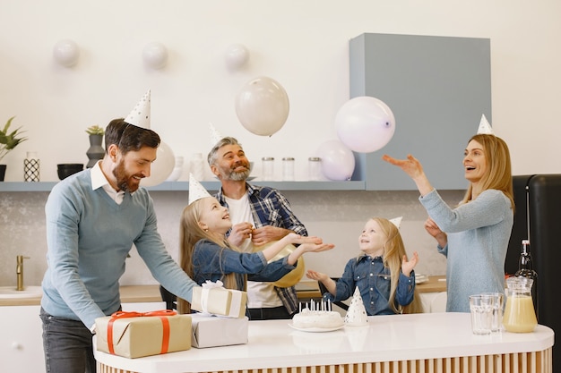 La familia y sus dos hijas tienen una celebración. La gente tiene globos. Los presentes están sobre la mesa.