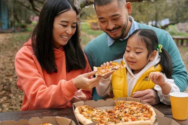 Familia de tiro medio comiendo pizza afuera