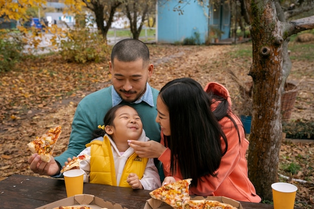 Familia de tiro medio con deliciosa pizza al aire libre.