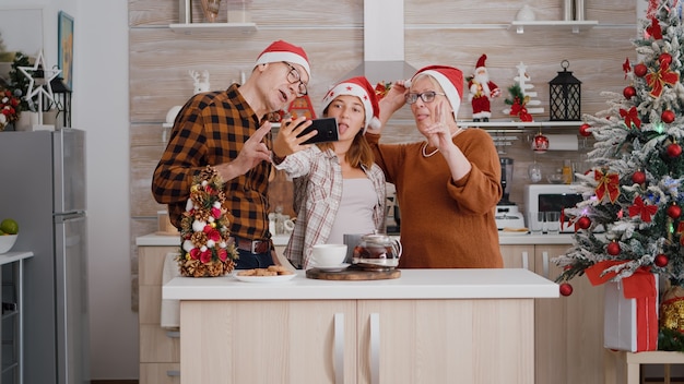 Familia tomando selfie con smartphone disfrutando de las vacaciones de invierno en la cocina decorada de Navidad