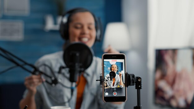 Famoso influencer de Internet filmando vlog diario con smartphone mientras cuenta historias de vida. Emocionado creador de contenido sentado en el escritorio del estudio en casa mientras transmite un blog de video. De cerca