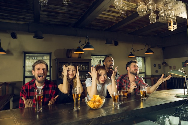 Foto gratuita fanáticos del deporte que animan en el bar, pub y beben cerveza mientras el campeonato, la competencia continúa