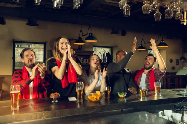 Los fanáticos del deporte vitoreando en el bar pub y bebiendo cerveza mientras se lleva a cabo la competencia del campeonato