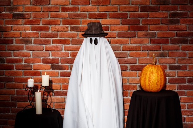 Foto gratuita fantasma con sombrero posando sobre la pared de ladrillo. fiesta de halloween.