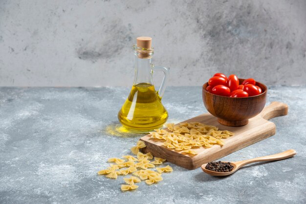 Farfalle crudo, tomates y aceite de oliva sobre tabla de madera.