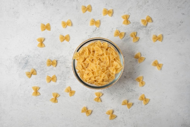 Farfalle de pasta en recipiente de vidrio sobre fondo blanco.