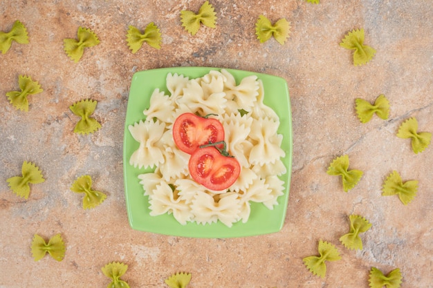 Farfalle con rodajas de tomate en placa verde.