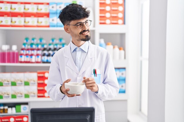Farmacéutico joven hispano sonriendo confiado trabajando en farmacia