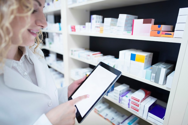 Foto gratuita farmacéutico sosteniendo la tableta por el estante lleno de medicamentos en la farmacia y verificando la disponibilidad y especificación de medicamentos