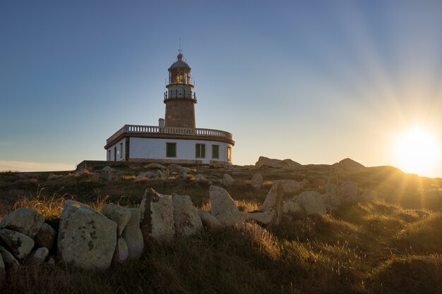 Faro de Corrubedo rodeado de rocas y césped bajo la luz del sol en España