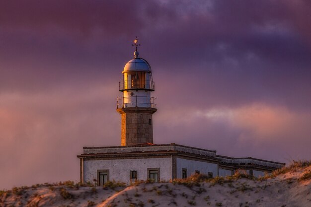 Faro de Larino bajo un cielo nublado durante la puesta de sol en la noche en España