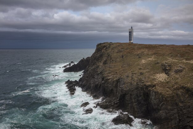 Faro de Meiras en los acantilados de Valdovino rodeado por el mar bajo un cielo nublado en Galicia, España