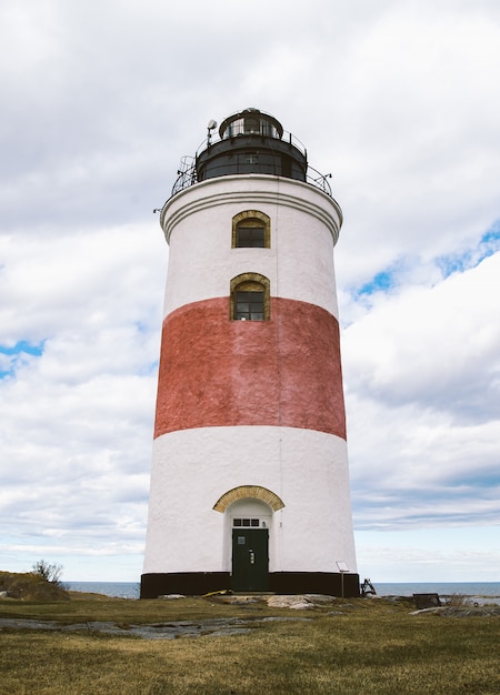 Faro rojo y blanco cerca del mar con un cielo nublado