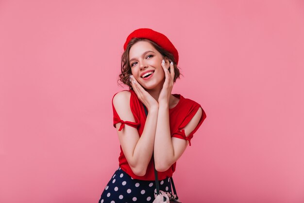 Fascinante modelo femenino francés posando con sonrisa interesada. chica romántica en traje rojo con boina.
