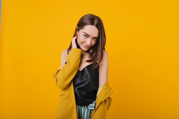 Fascinante mujer caucásica que expresa verdaderas emociones positivas. Retrato de interior de niña complacida con cabello castaño sonriendo.