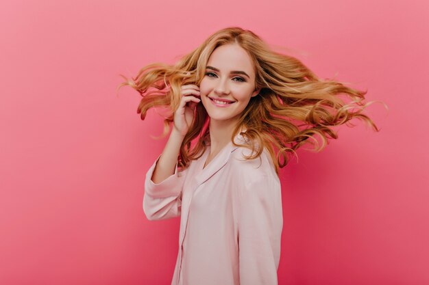 Fascinante mujer pálida en pijama rosa claro que expresa felicidad. adorable dama en lindo camisón riendo en una pared brillante.