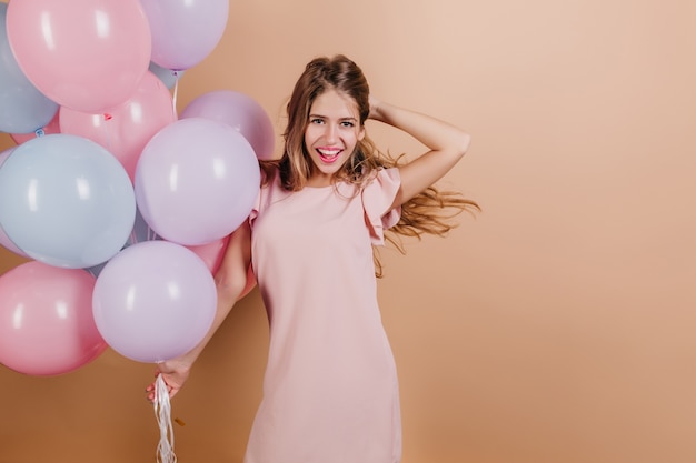 Fascinante mujer sonriente jugando con su cabello mientras posa en la fiesta