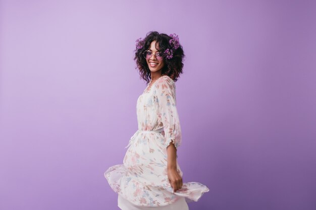 Fascinante niña africana con flores en el pelo posando. Modelo femenino negro de moda en vestido de baile.