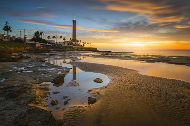 Fascinante vista de un hermoso paisaje marino con un faro en la pintoresca puesta de sol colorida