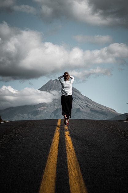 Fascinante vista de un joven turista caminando por la carretera vacía que conduce a la montaña