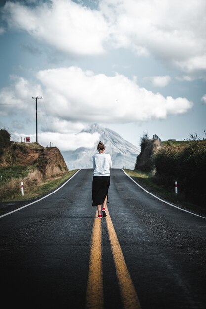 Fascinante vista de un joven turista caminando por la carretera vacía que conduce a la montaña